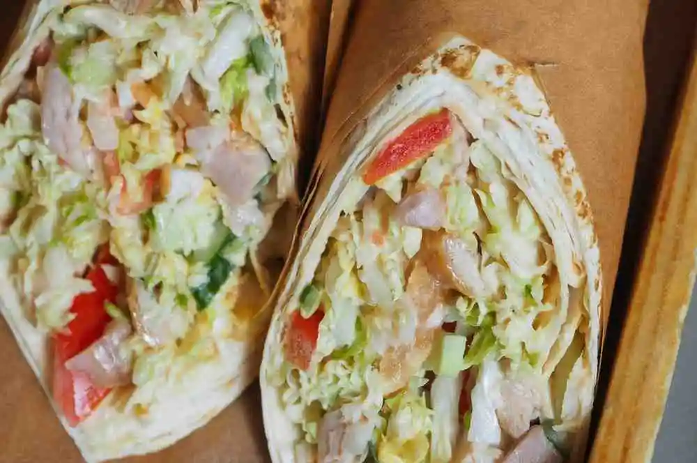 Shredded BBQ chicken and coleslaw wraps cut in half wrapped in paper
