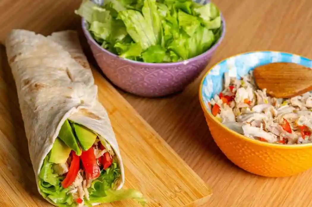 Freshly prepared chicken wrap with ingredients and coleslaw bowl