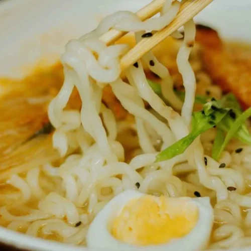 Lifting ramen noodles with chopsticks from a warm bowl of spicy chicken soup