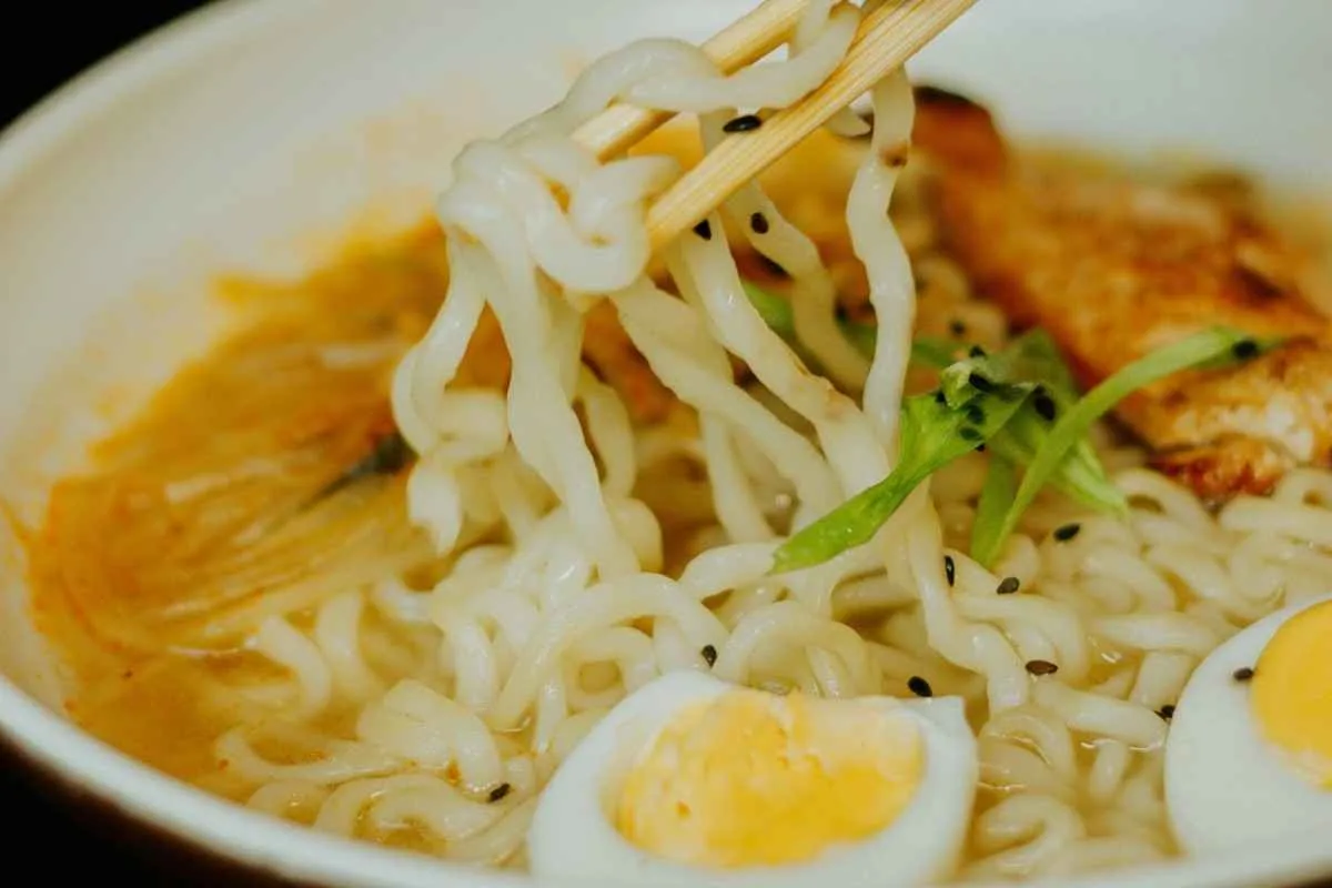 Lifting ramen noodles with chopsticks from a warm bowl of spicy chicken soup