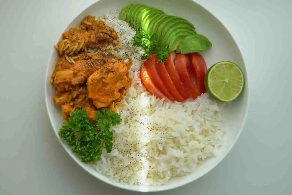 Plated grilled chicken avocado rice bowl with sliced cucumbers and lime