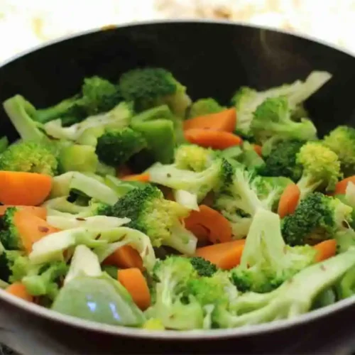 Fresh broccoli slaw mix and chopped vegetables sautéing in a pan