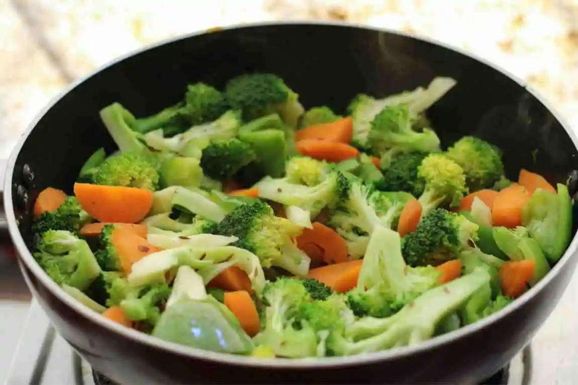 Fresh broccoli slaw mix and chopped vegetables sautéing in a pan