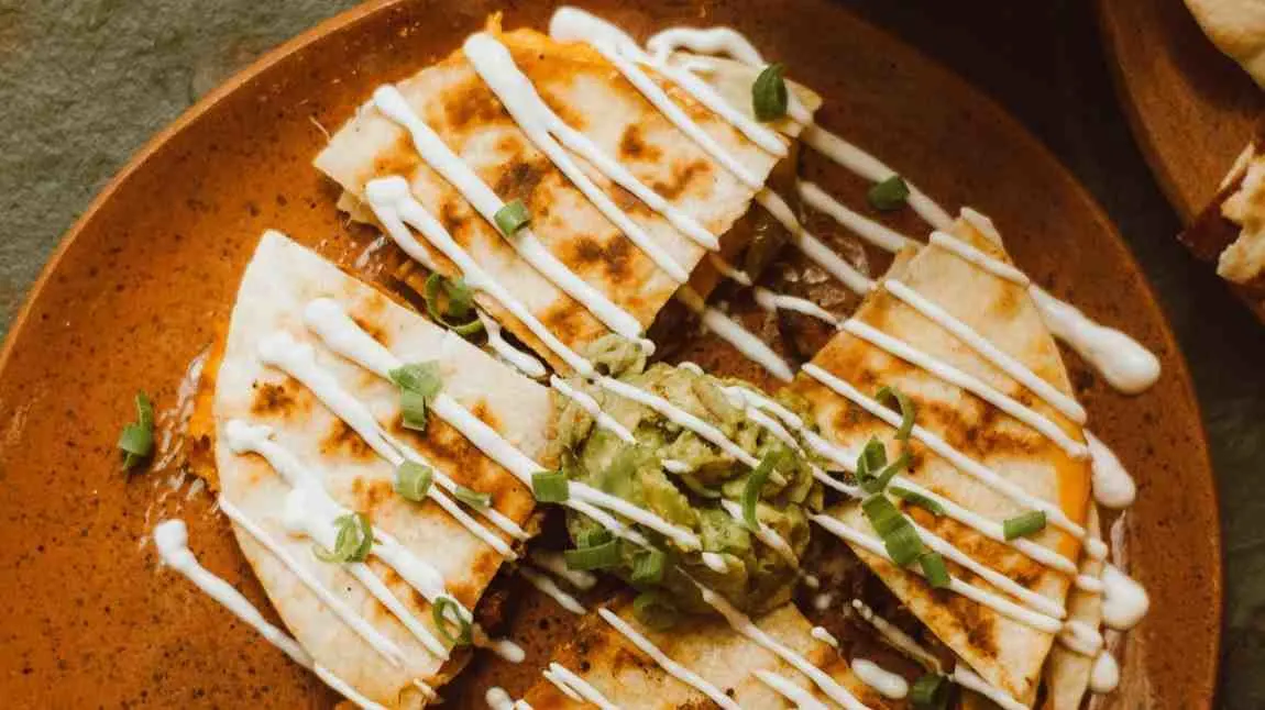 Crispy skillet ground beef quesadilla sliced with sour cream and salsa