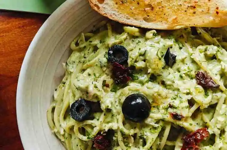 Creamy green pesto pasta served with garlic bread and black olives