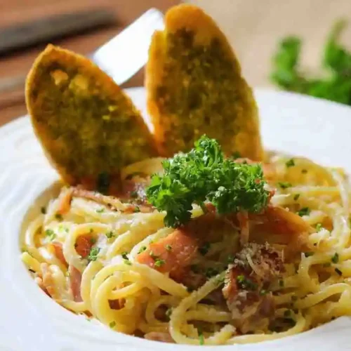 Plated white cream sauce pasta with garlic bread toast on a white plate