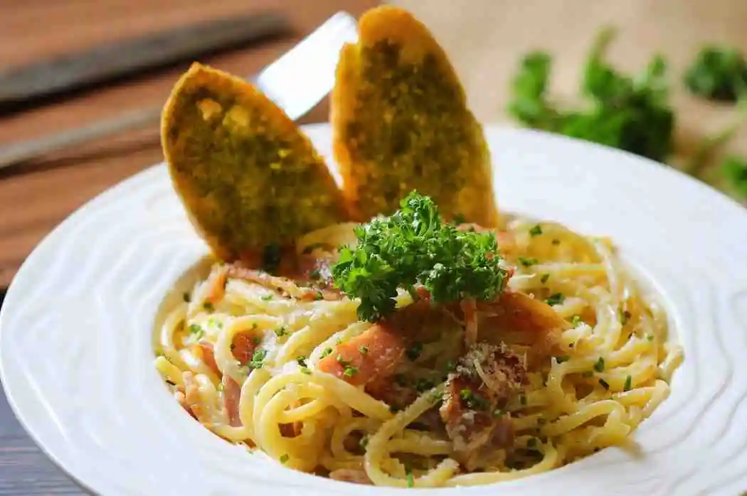 Plated white cream sauce pasta with garlic bread toast on a white plate