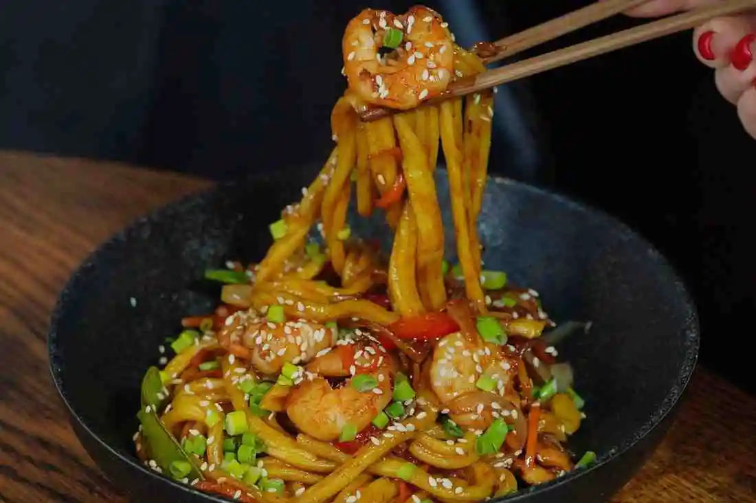 Keto steak and shrimp stir fry served over low carb shirataki noodles topped with sesame seeds and green onions.