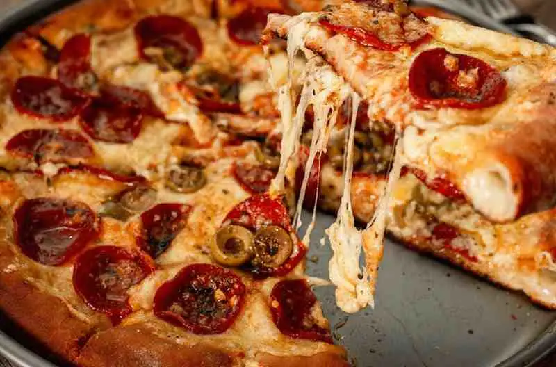 Lifting a slice of cheesy low carb pizza casserole with melted mozzarella and pepperoni