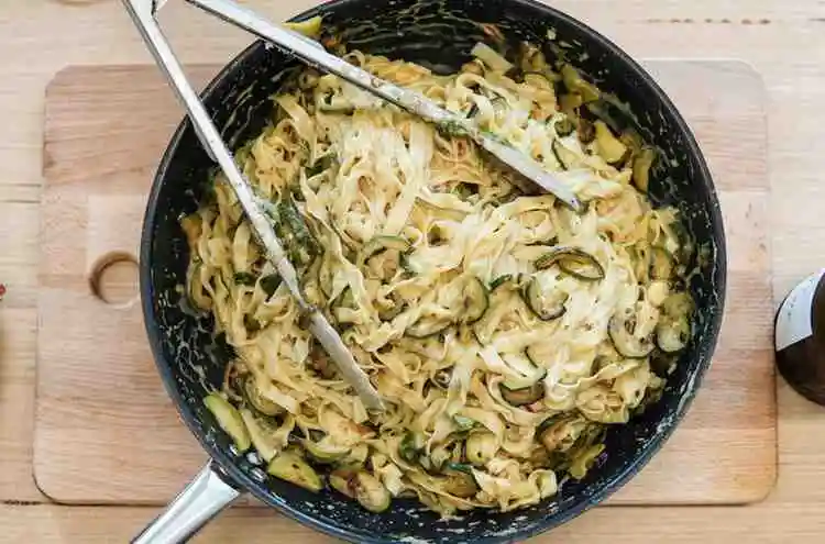 Cooking keto chicken alfredo with zucchini noodles in a skillet
