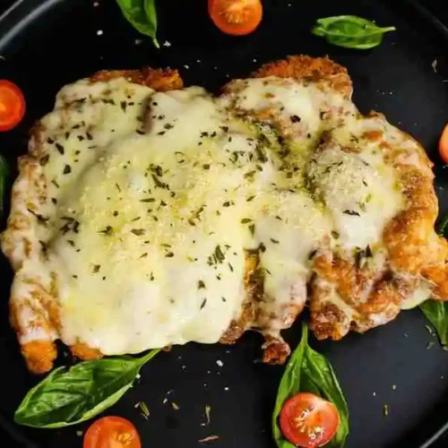 Keto chicken parmesan garnished with fresh basil leaves on a black plate