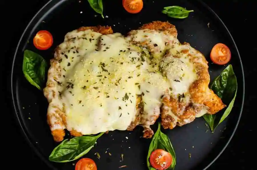 Keto chicken parmesan garnished with fresh basil leaves on a black plate