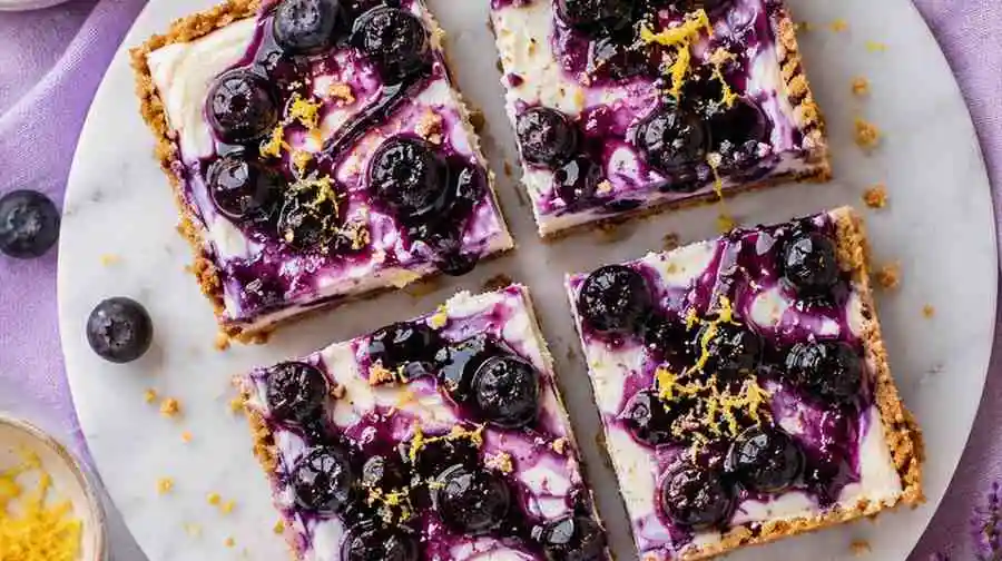 Four fresh blueberry cream cheese bars cut into square slices served on a white marble plate.