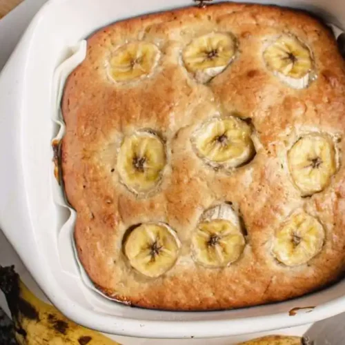 Freshly baked banana bread brownies topped with banana slices served in a white baking dish.