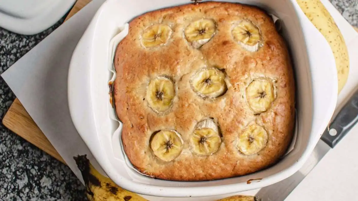 Freshly baked banana bread brownies topped with banana slices served in a white baking dish.
