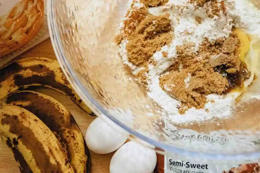 Baking ingredients for banana bread brownies including ripe bananas, eggs, flour, and brown sugar.