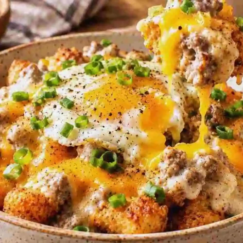 Tater tot breakfast bowl with sausage gravy melted cheddar cheese and fried egg on a fork